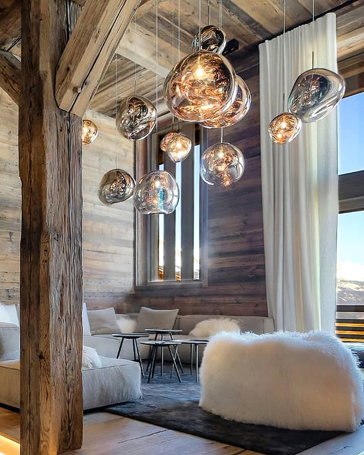 A cluster of Clérachic glass pendants in copper, gold and silver, hanging in a chalet lounge with a timber beam and a fur pouffe.