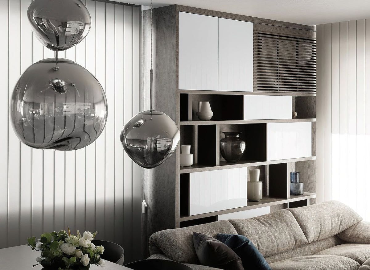 Two Clérachic silver glass pendants hanging in a room with white panelling, with a grey sofa and a vase of flowers below.