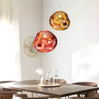 Two Clérachic glass pendants, one copper-red and one gold, above a tabletop with glasses, in front of a white wall.
