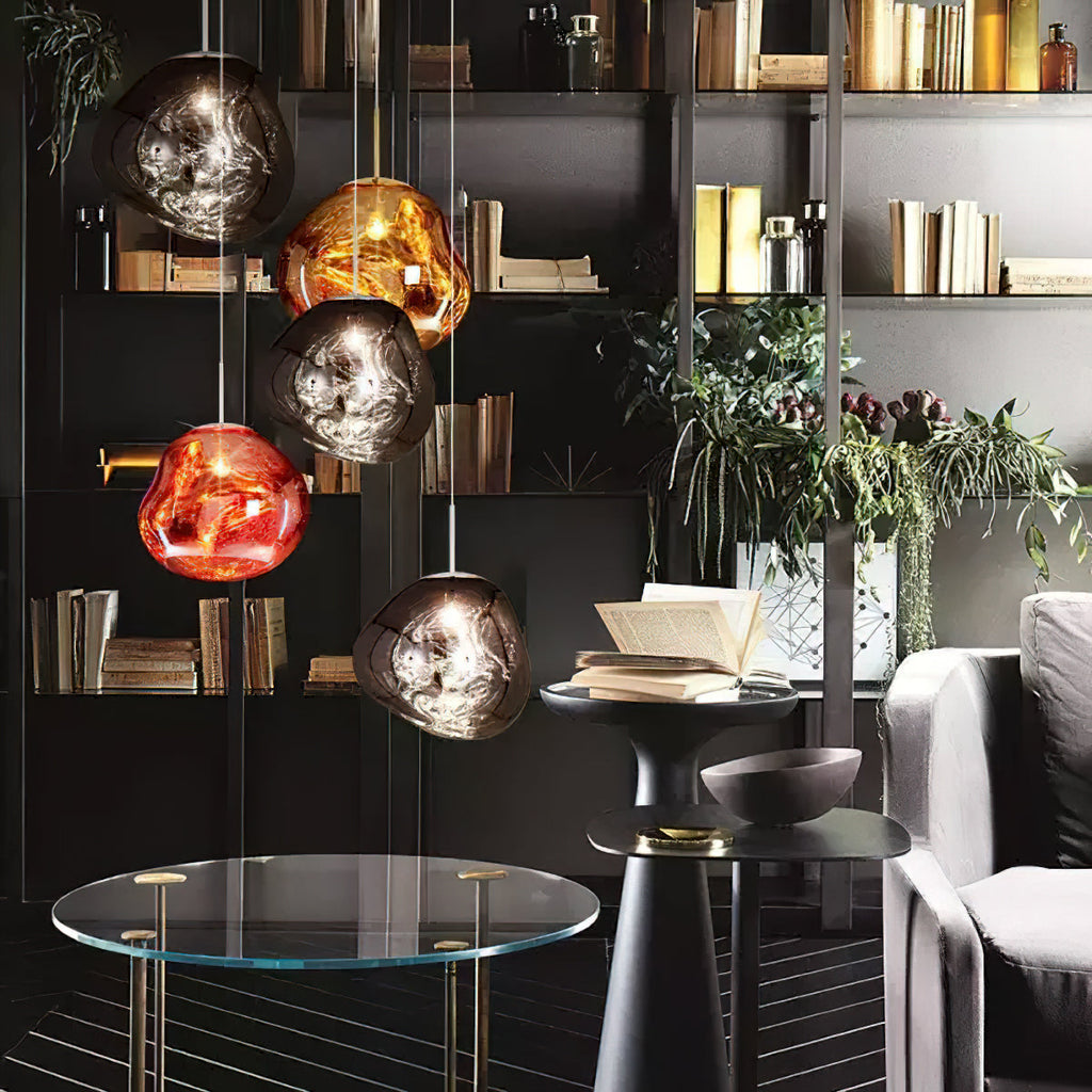A Clérachic group of glass pendants, in copper, gold and smoke tones, in front of dark bookshelves and a glass side table.