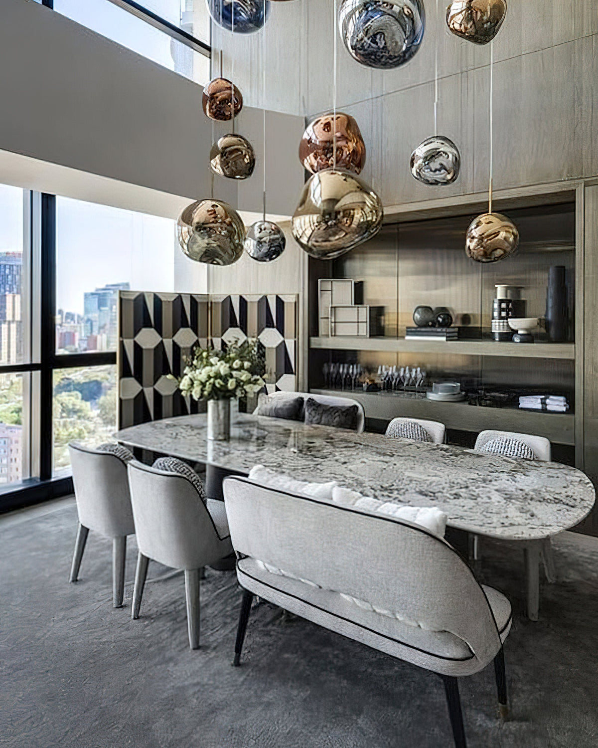 Many Clérachic glass pendants, copper, gold and silver, hang in a tall room above a marble table and upholstered chairs.