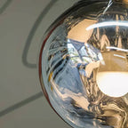 A Clérachic silver glass pendant seen up close, with its curved surface and a pale bulb reflected inside the glass.