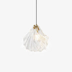 A Clérachic shell-shaped glass pendant with a brass cap hangs from a black cord, its ribbed clear glass lit on a plain white backdrop.