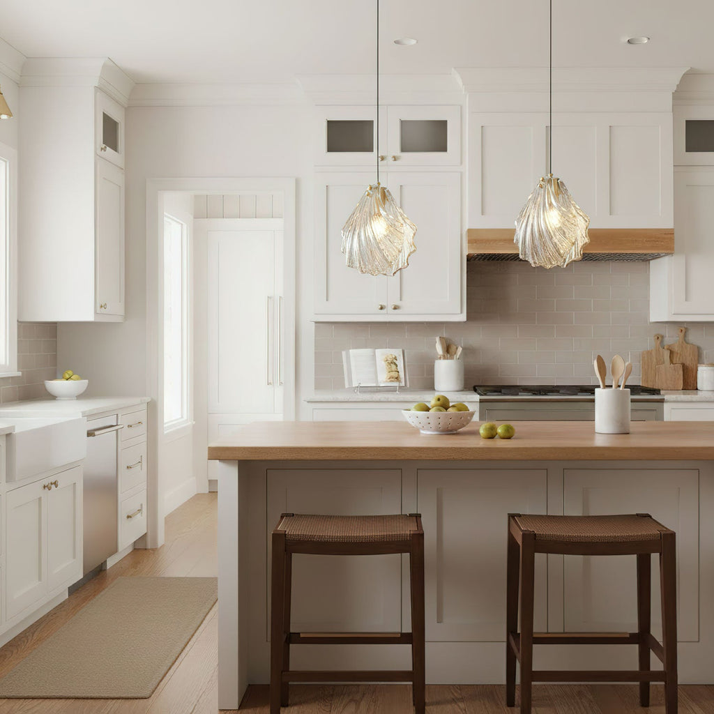 Two ribbed glass Clérachic pendants hang over a timber-topped kitchen island with two dark-wood stools in a white kitchen.