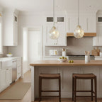 Two ribbed glass Clérachic pendants hang over a timber-topped kitchen island with two dark-wood stools in a white kitchen.