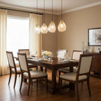 A row of four Clérachic glass shell pendants glows above a dark wood dining table laid with glasses and white flowers.
