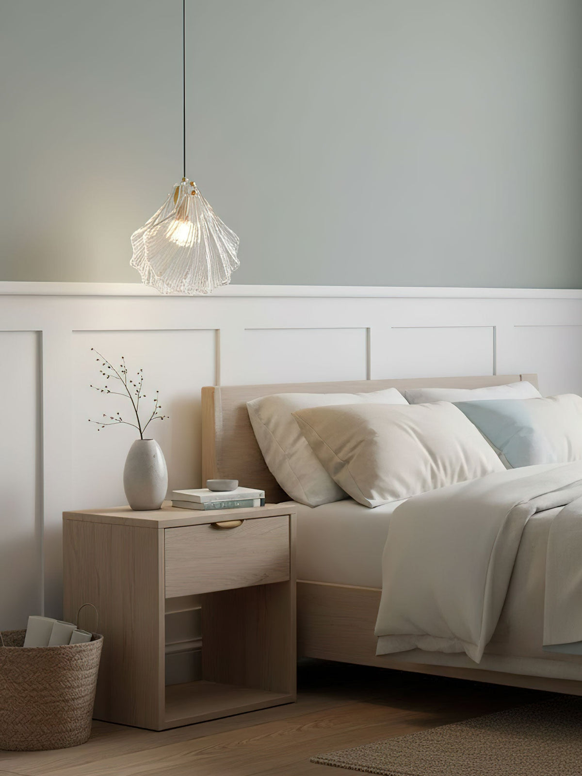 Above a pale wooden bedside table, a Clérachic clear glass shell pendant hangs against a soft green-grey wall and white panelling.