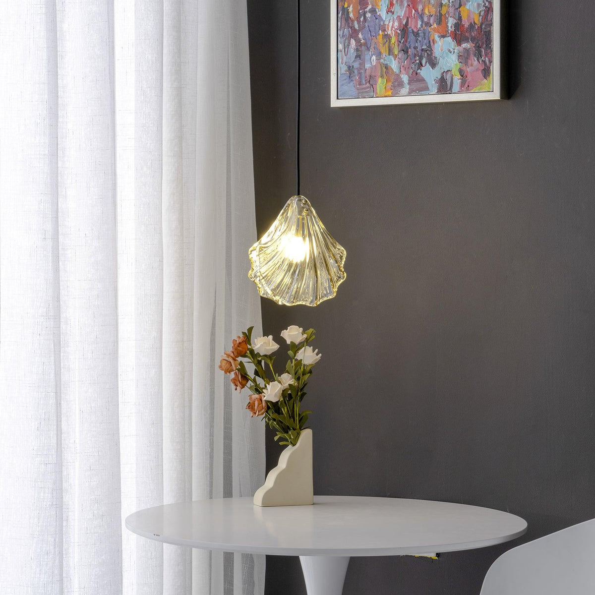 A Clérachic ribbed glass pendant in a warm amber tone hangs against a charcoal wall beside a sheer curtain and a white round table.
