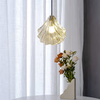 Close view of a Clérachic shell pendant in warm cognac glass, lit, with a vase of peach and white roses below it.