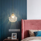 A Clérachic clear glass shell pendant throws soft light across a teal slatted wall above a pink velvet headboard.