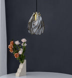 A Clérachic pendant in a darker, smoke-toned version of the twisted glass shade hangs above a vase of roses on a charcoal wall.