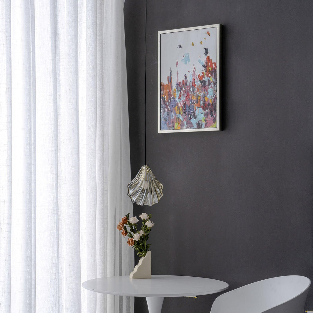 Wide view of a Clérachic shell pendant hanging low beside a framed abstract print, with a vase of flowers on a white table.