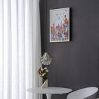 Wide view of a Clérachic shell pendant hanging low beside a framed abstract print, with a vase of flowers on a white table.