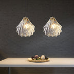 Two Clérachic shell pendants with ribbed clear glass glow side by side over a pale table holding a dish of decorative eggs.