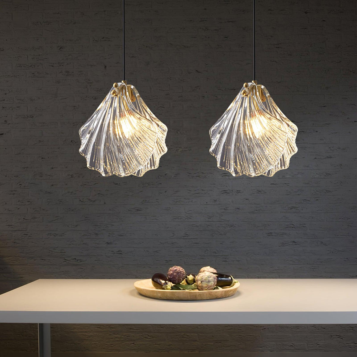 Two Clérachic shell pendants with ribbed clear glass glow side by side over a pale table holding a dish of decorative eggs.