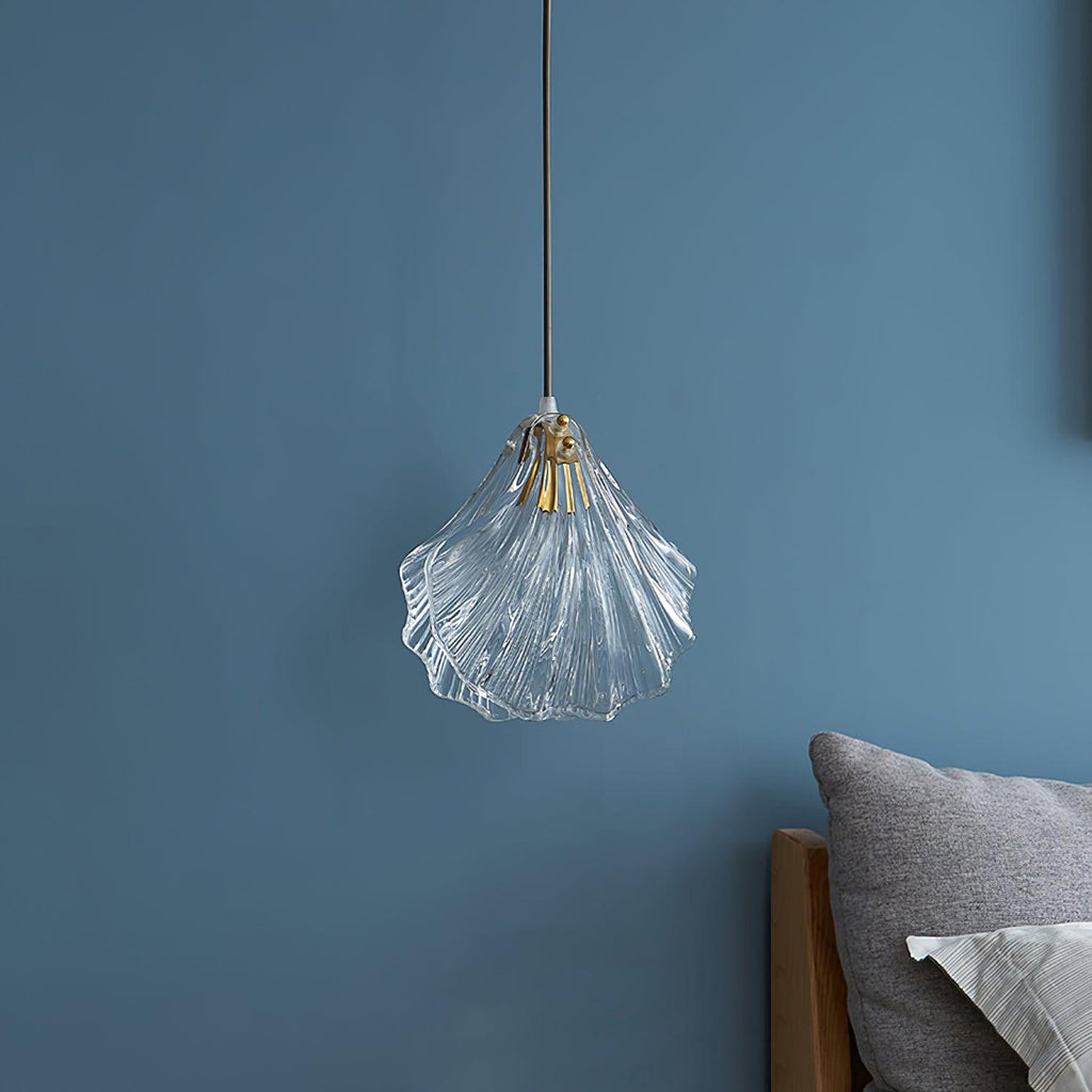 The same Clérachic shell pendant switched off, showing clear glass ribs and a brass fitting against a blue wall.