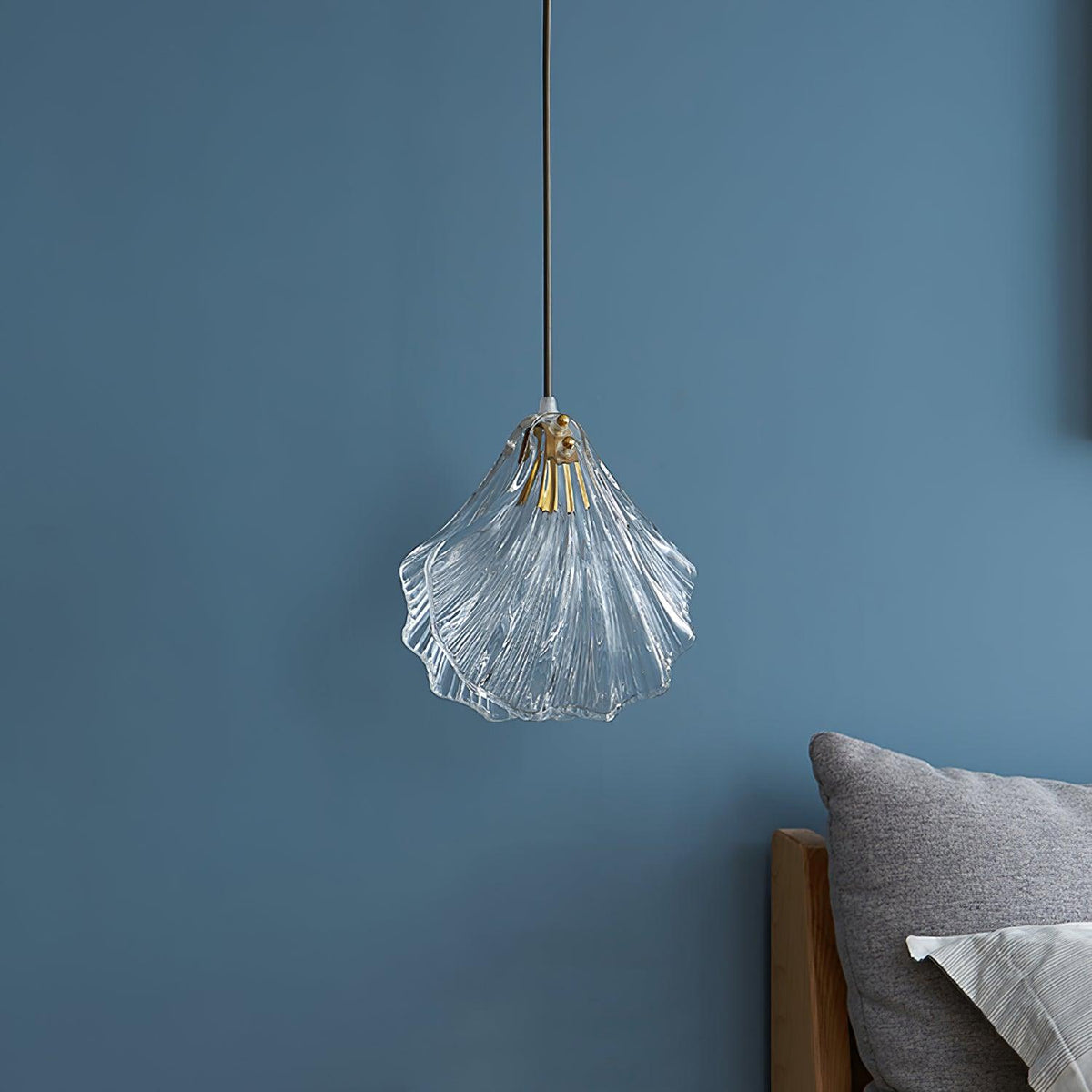 The same Clérachic shell pendant switched off, showing clear glass ribs and a brass fitting against a blue wall.
