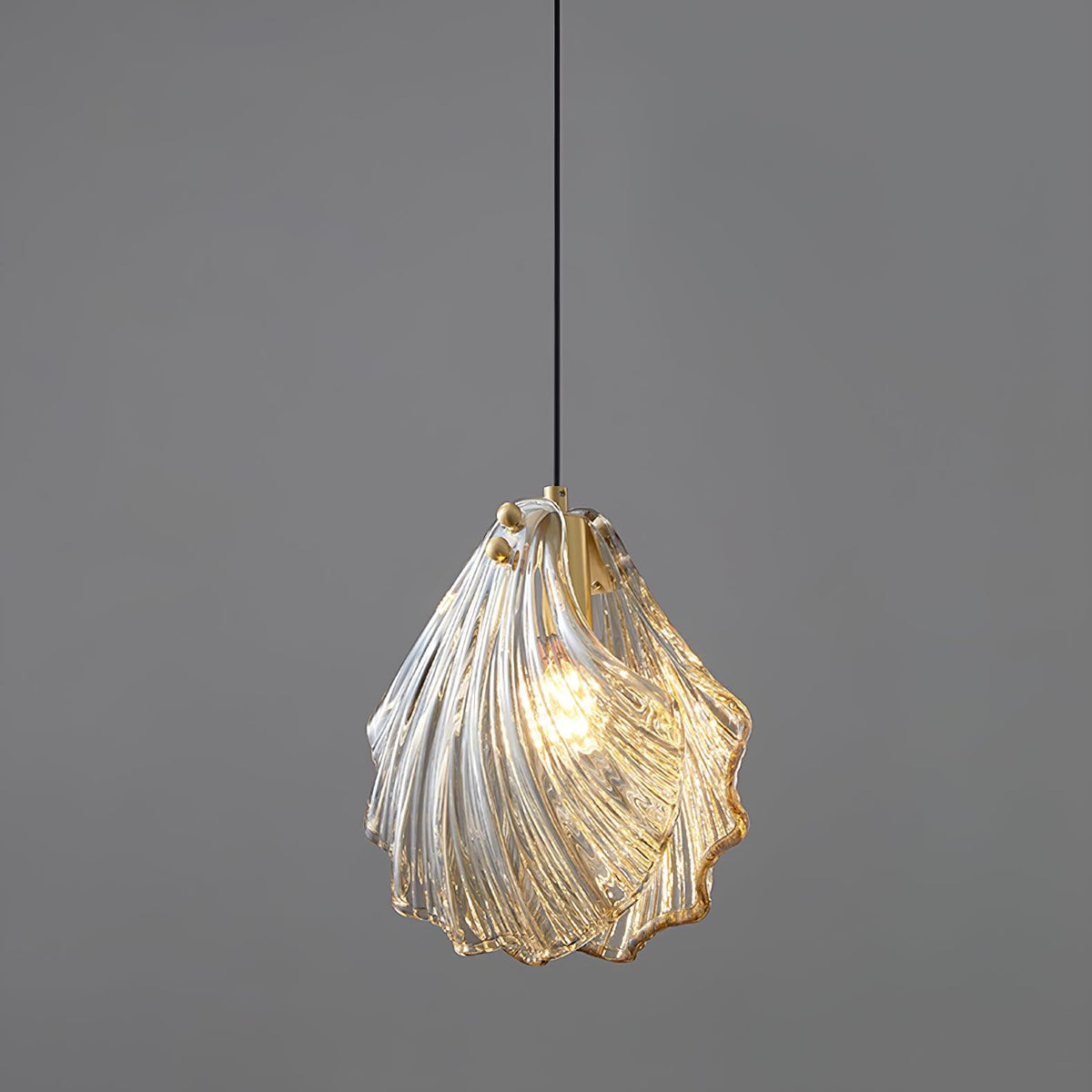 A Clérachic pendant with a twisted, overlapping glass shade in clear and amber tones, lit on a plain grey backdrop.