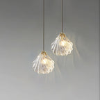 Two Clérachic shell pendants at different heights glow against a pale grey backdrop, each with a small brass top.