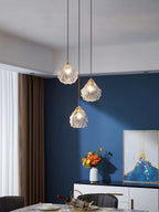 Three Clérachic shell pendants hang at different heights in front of a blue wall, with an abstract picture and flowers below.