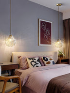 A pair of Clérachic shell pendants hangs either side of a bed, lighting a soft grey wall and a framed line drawing.