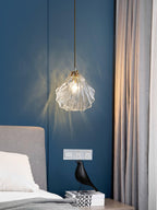 A Clérachic shell pendant hangs over a bedside stack of books and a black bird figure, against a navy wall.