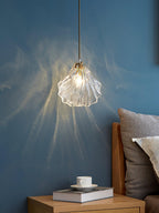 A Clérachic shell pendant fills a blue wall with rays of light above a wood bedside table, a coffee cup and a book.