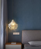 A Clérachic shell pendant hangs by a grey curtain and a grey upholstered headboard, against a deep blue textured wall.