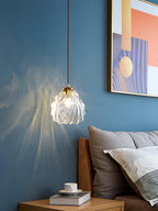 A Clérachic shell pendant hangs beside a framed pastel print on a blue wall, above a bedside cup of tea and a book.