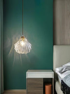 A Clérachic ribbed glass pendant glows against a deep green wall beside a white and wood dressing table and a bed.