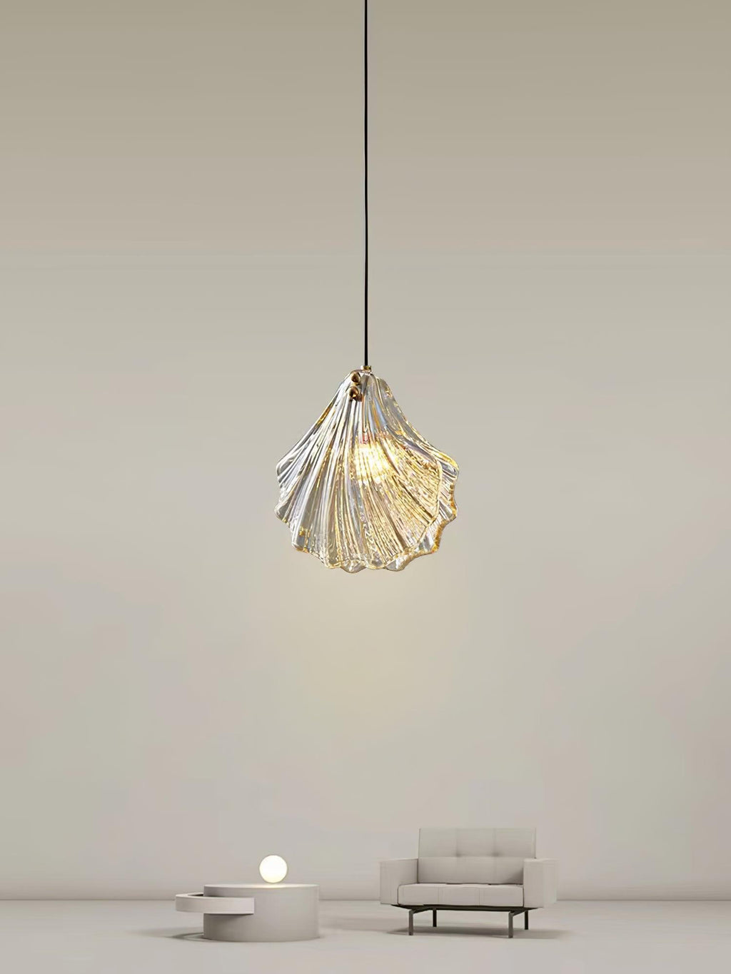 A Clérachic shell pendant hangs high in a pale, minimal room, with a small sofa and a low round table far below.