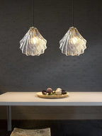 Two Clérachic ribbed glass pendants hang side by side against a dark textured wall, above a pale bench with a bowl on it.
