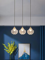 Three Clérachic shell pendants hang in a line from one ceiling plate, in front of a navy wall with a framed print.