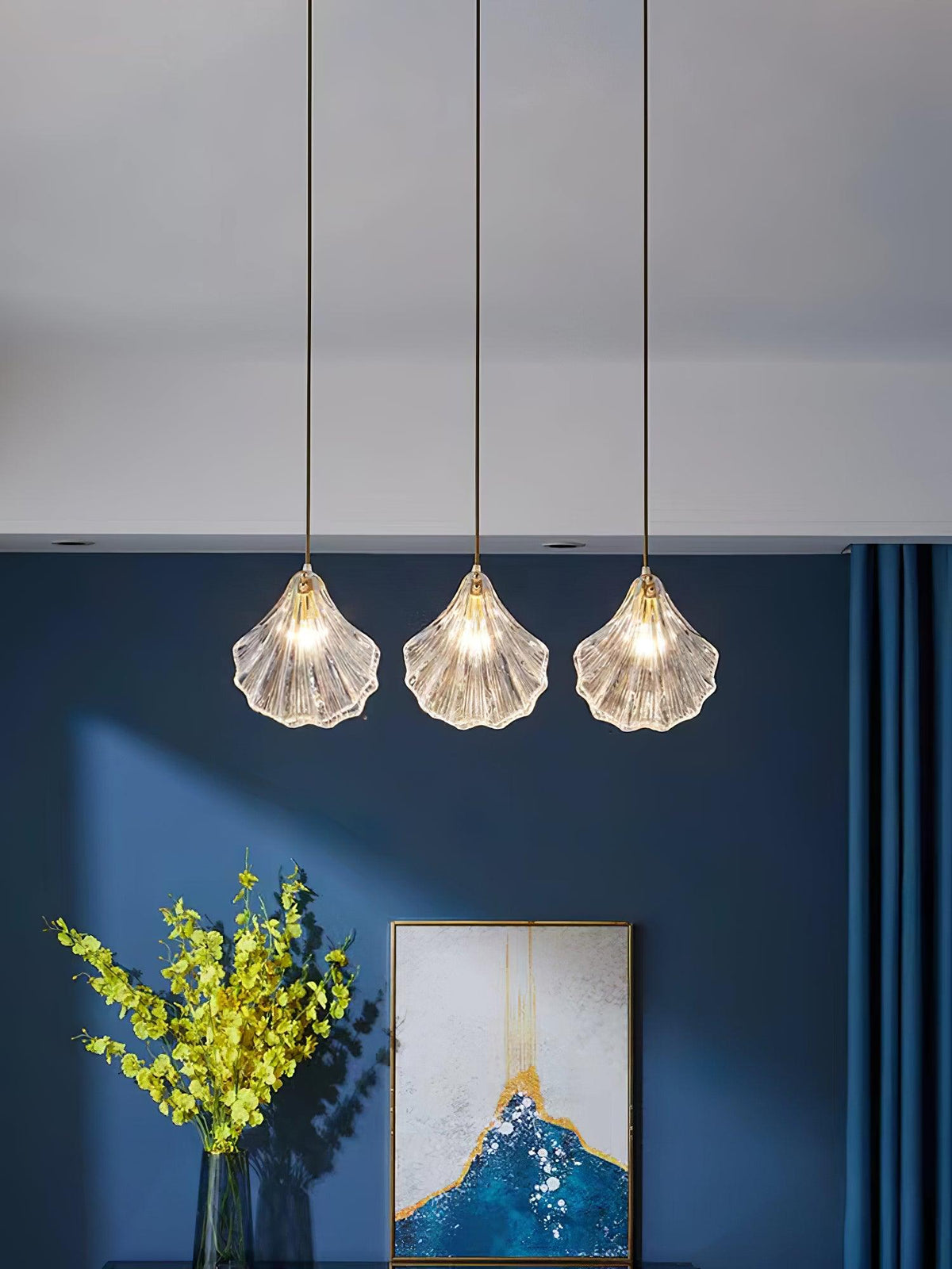 Three Clérachic shell pendants hang in a line from one ceiling plate, in front of a navy wall with a framed print.