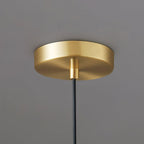 Close view of the round brushed brass ceiling plate and black cord of this Clérachic pendant, against a grey backdrop.