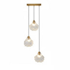A Clérachic three-light pendant with clear glass shells hangs at three lengths from a straight brass bar, on white.