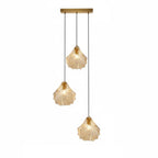 A Clérachic three-light pendant with cognac glass shells hangs at three lengths from a straight brass bar, on white.
