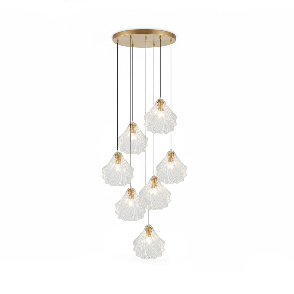 A Clérachic cluster of seven clear glass shell pendants hangs at staggered lengths from a round brass plate, on white.