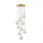 A Clérachic cluster of nine clear glass shell pendants hangs at different lengths from a round brass ceiling plate.
