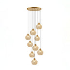 A Clérachic cluster of nine cognac glass shell pendants hangs at different lengths from a round brass ceiling plate.
