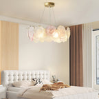 A lit Clérachic ring pendant hangs above a bed with a white buttoned headboard and a brown curtain beside it.