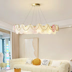 Clérachic pendant with pearl swags and glass discs, lit, hung in a living room above a cream sofa with a yellow cushion.