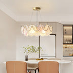 A Clérachic pearl-swagged glass-disc pendant in a bright dining area, with a white table and tan chairs under it.