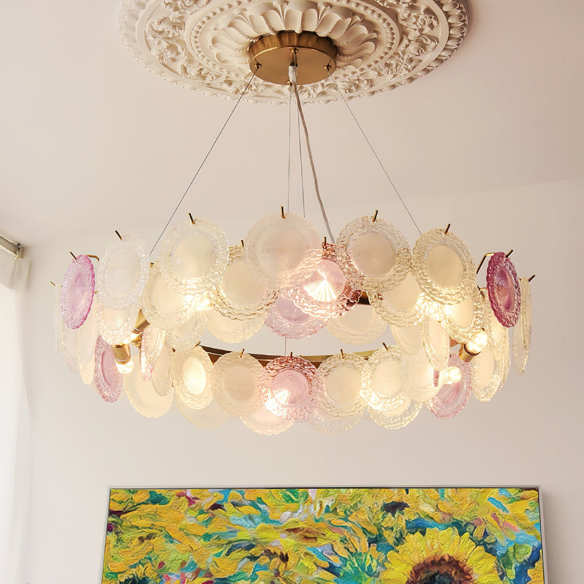 This Clérachic pendant hangs from an ornate plaster ceiling rose, with two rows of pink and frosted glass discs and a sunflower painting below.