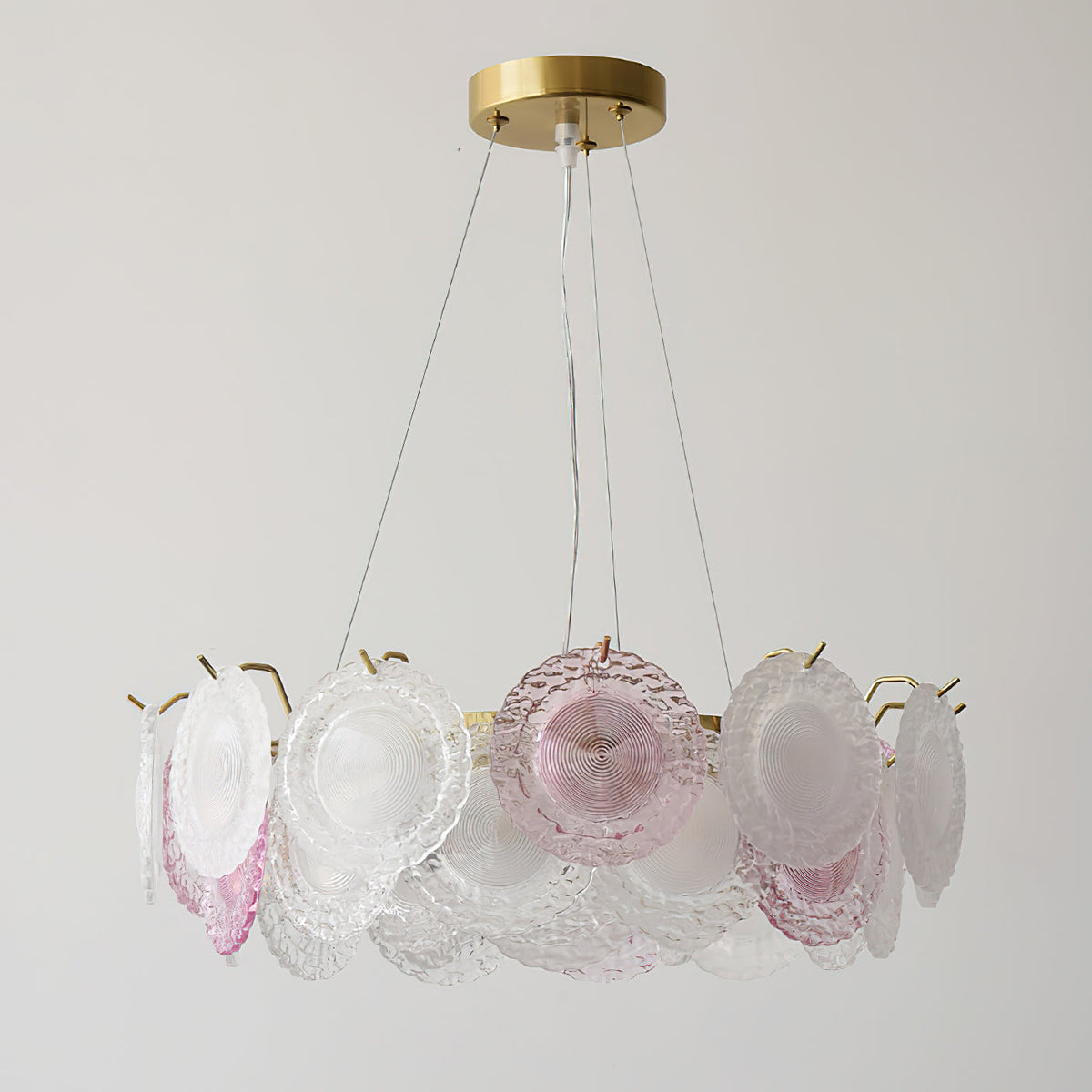 A Clérachic ring pendant of frosted and pink glass discs on a brass canopy, unlit, against a light grey wall.