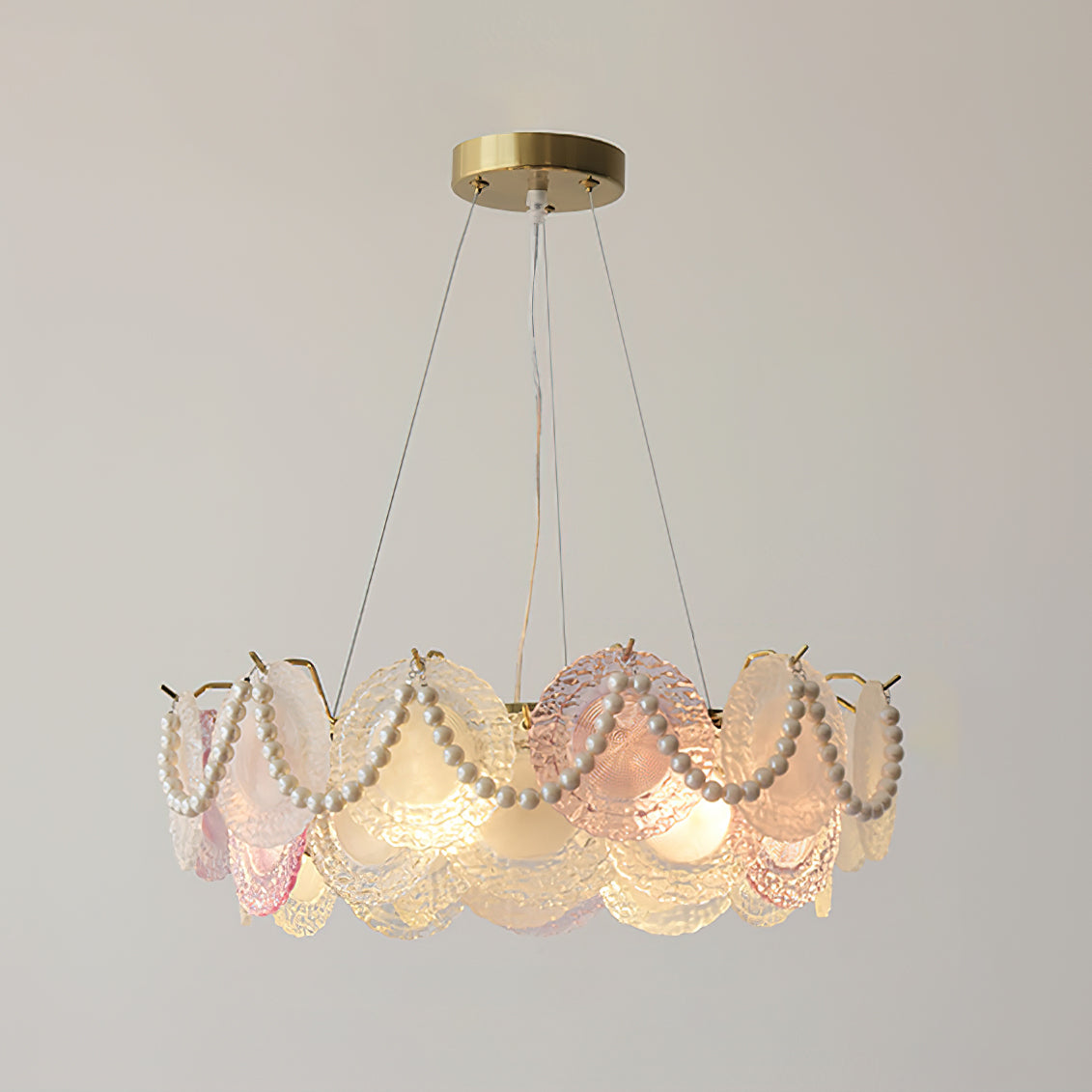 Clérachic pendant with pearl swags across the discs, lit, on a brass canopy against a grey-beige wall.