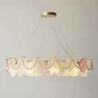 Wide Clérachic pendant with pearl swags, lit, with a ring of frosted glass discs and a few pink ones on a grey wall.