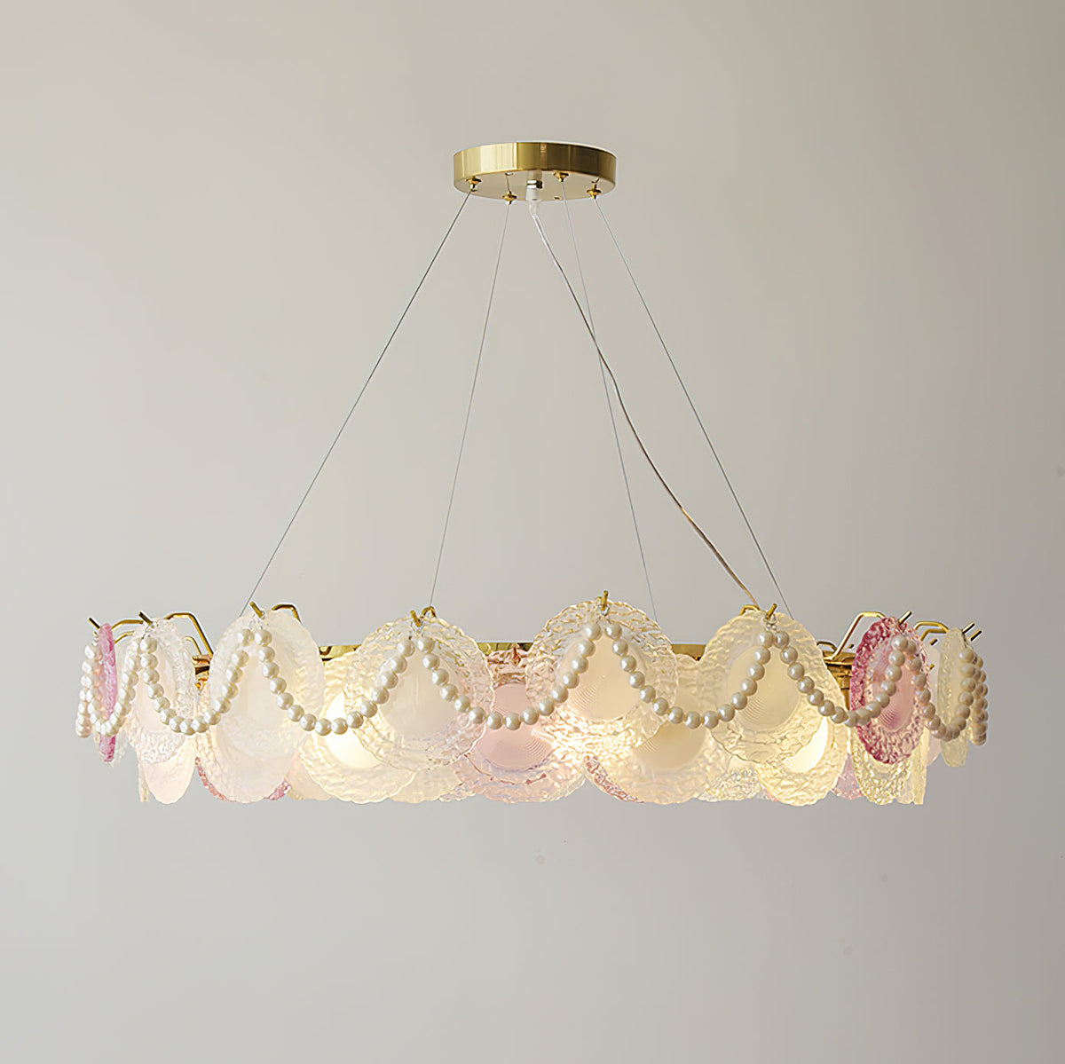 A wide Clérachic pendant with looped pearls and glass discs, lit, with the three suspension wires visible above it.