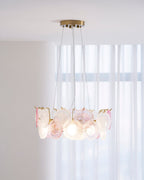 A Clérachic ring pendant glowing in a bright room, with sheer curtains behind it and a table below.
