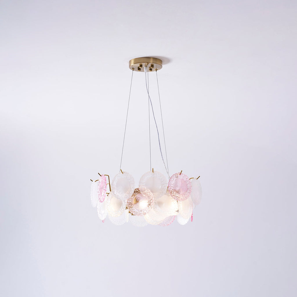 A Clérachic pendant with pink and frosted glass discs, lit, hung on three wires against a pale lilac wall.